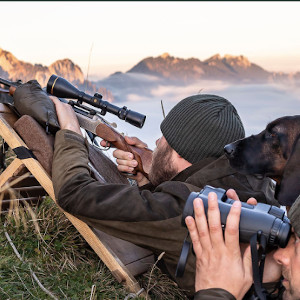 På jagt i bjergene. To jægere ligger med riffel og kikkert og venter.