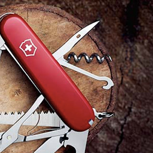 Rød Victorinox schweizerkniv udfoldet på træstamme der er skåret over. Værktøjer udfoldet. 