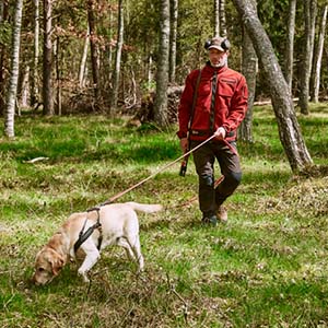 Jæger iført jagtbukser og jagtjakke med sin hund i snor